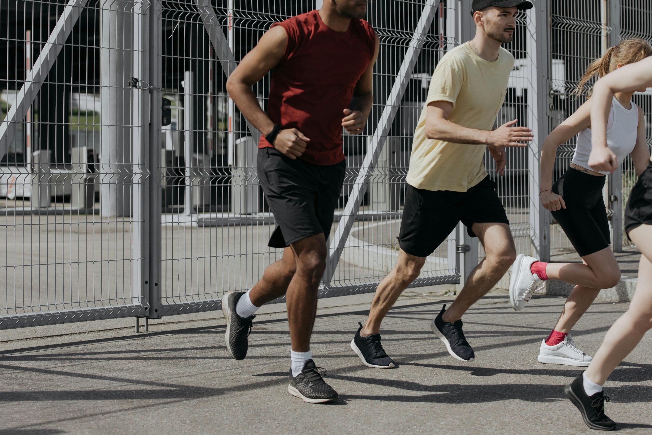 Energetic group of people running together outdoors under bright sunlight, wearing comfortable sportswear.