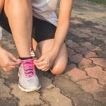 Adult woman tying pink laces on running shoes outdoors. Focuses on fitness and lifestyle.