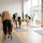 A diverse group performing yoga forward bend pose in a bright yoga studio.